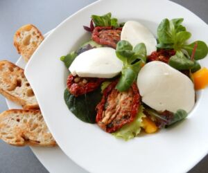 Salát s mozarellou, sušenými rajčaty a bagetkou na česnekovém másle